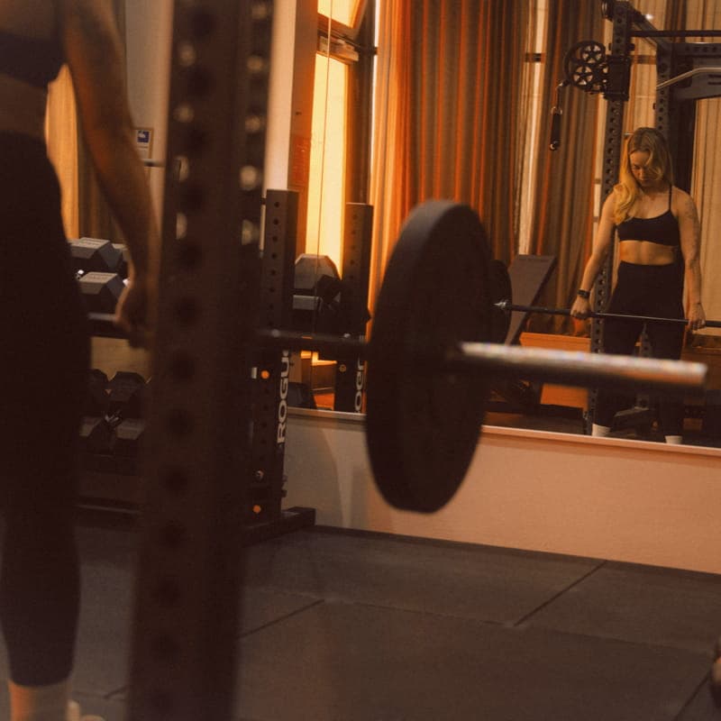 Eine beladene Langhantel im Rogue-Rack im SHIO Private Gym, die Athletin spiegelt sich im Studiospiegel
